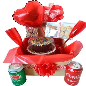 Cesta Festa na Caixa com bolo confeitado, docinhos, salgadinhos, refrigerantes, taças decorativas e balão em formato de coração.